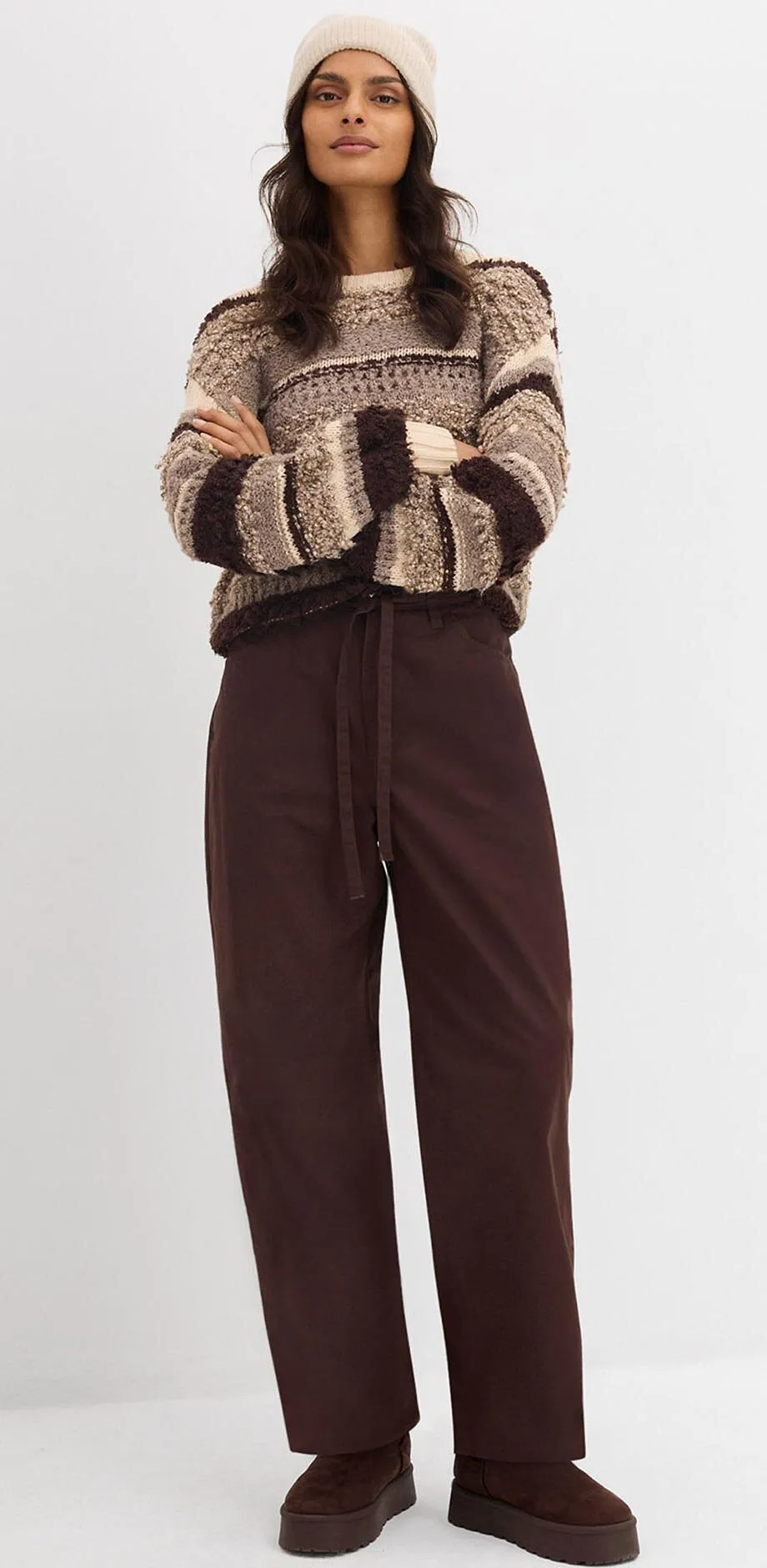 Pull en maille beige et marron avec un pantalon marron.
