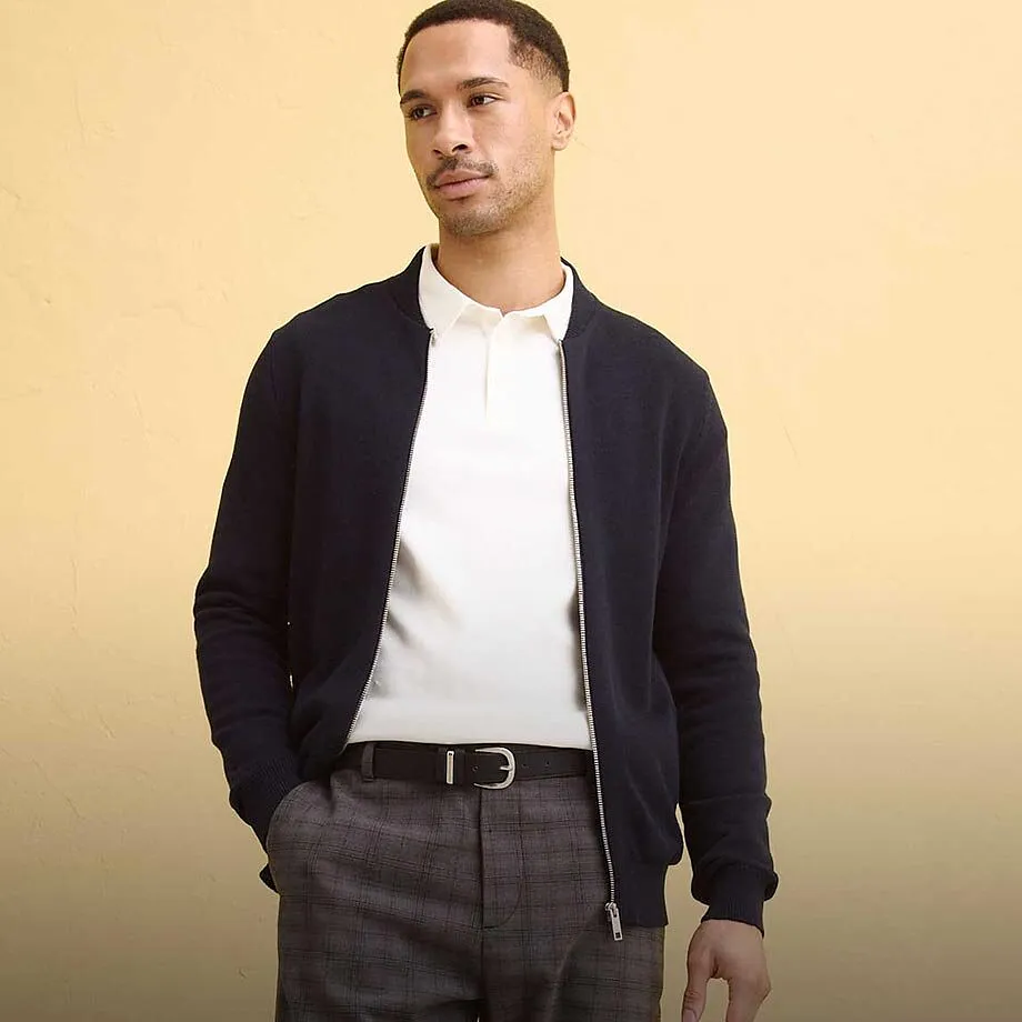 Dunkle Strickjacke &uuml;ber wei&szlig;em Poloshirt, kombiniert mit grauer Hose.