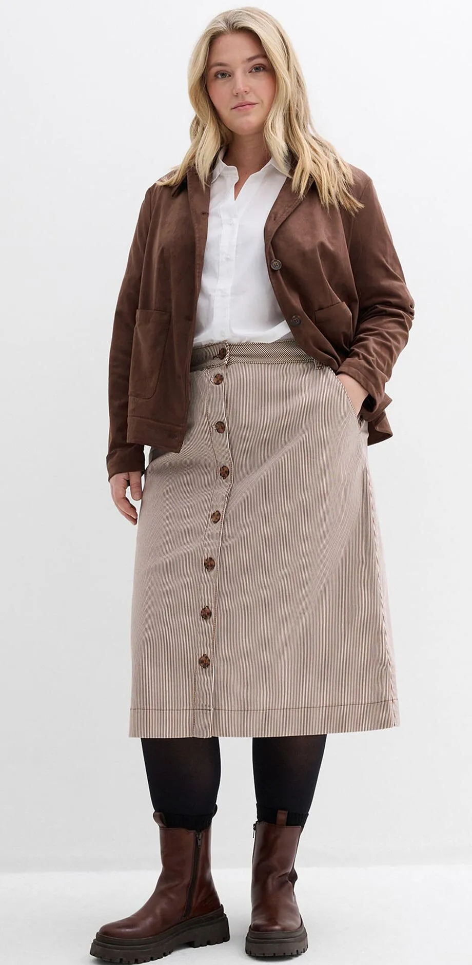 Braune Jacke, wei&szlig;e Bluse, gestreifter Knopfrock und braune Boots.
