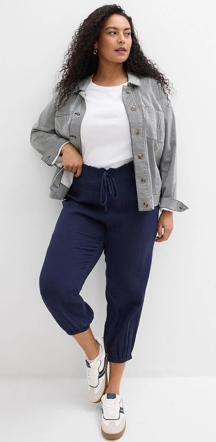 Graue Jacke &uuml;ber wei&szlig;em Top, dunkelblaue Hose und wei&szlig;e Sneakers.