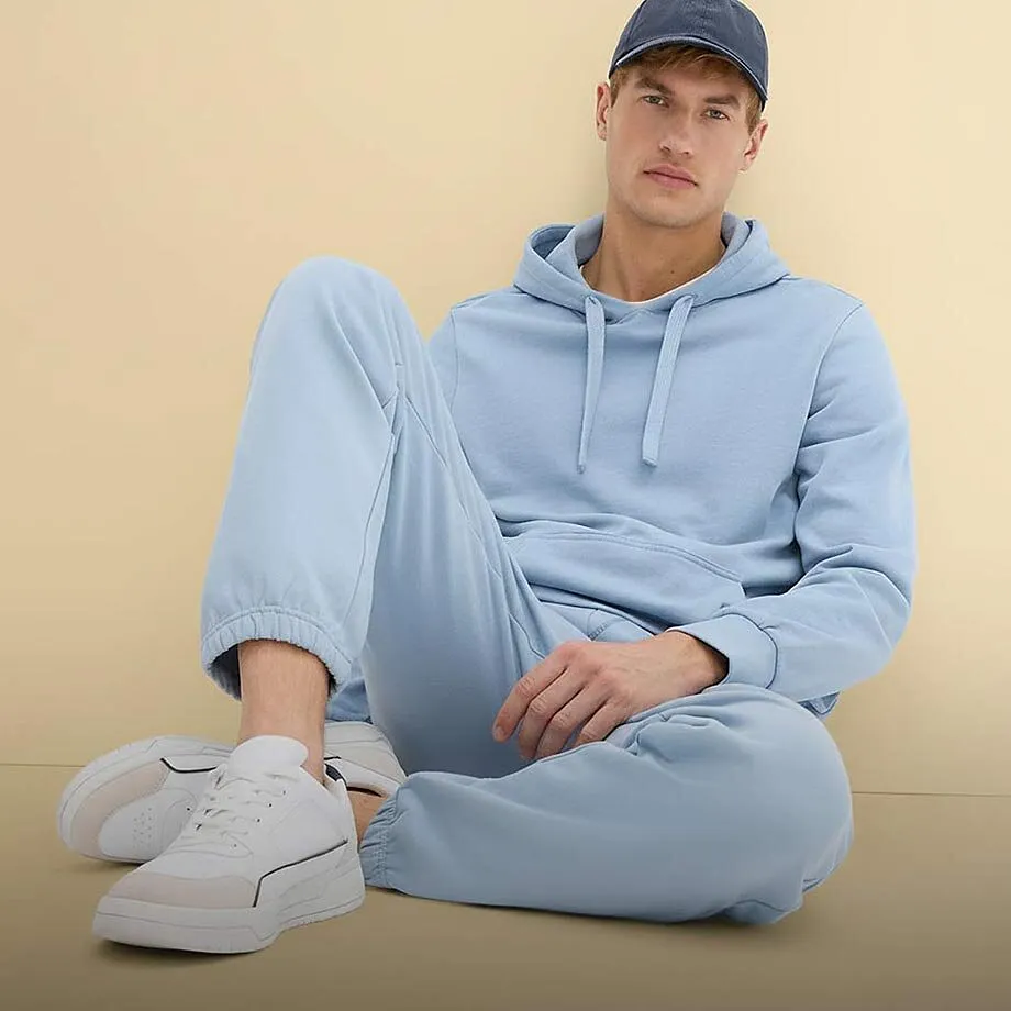 Hellblauer Kapuzenpullover und Jogginghose, erg&auml;nzt durch wei&szlig;e Sneaker und blaue Kappe.