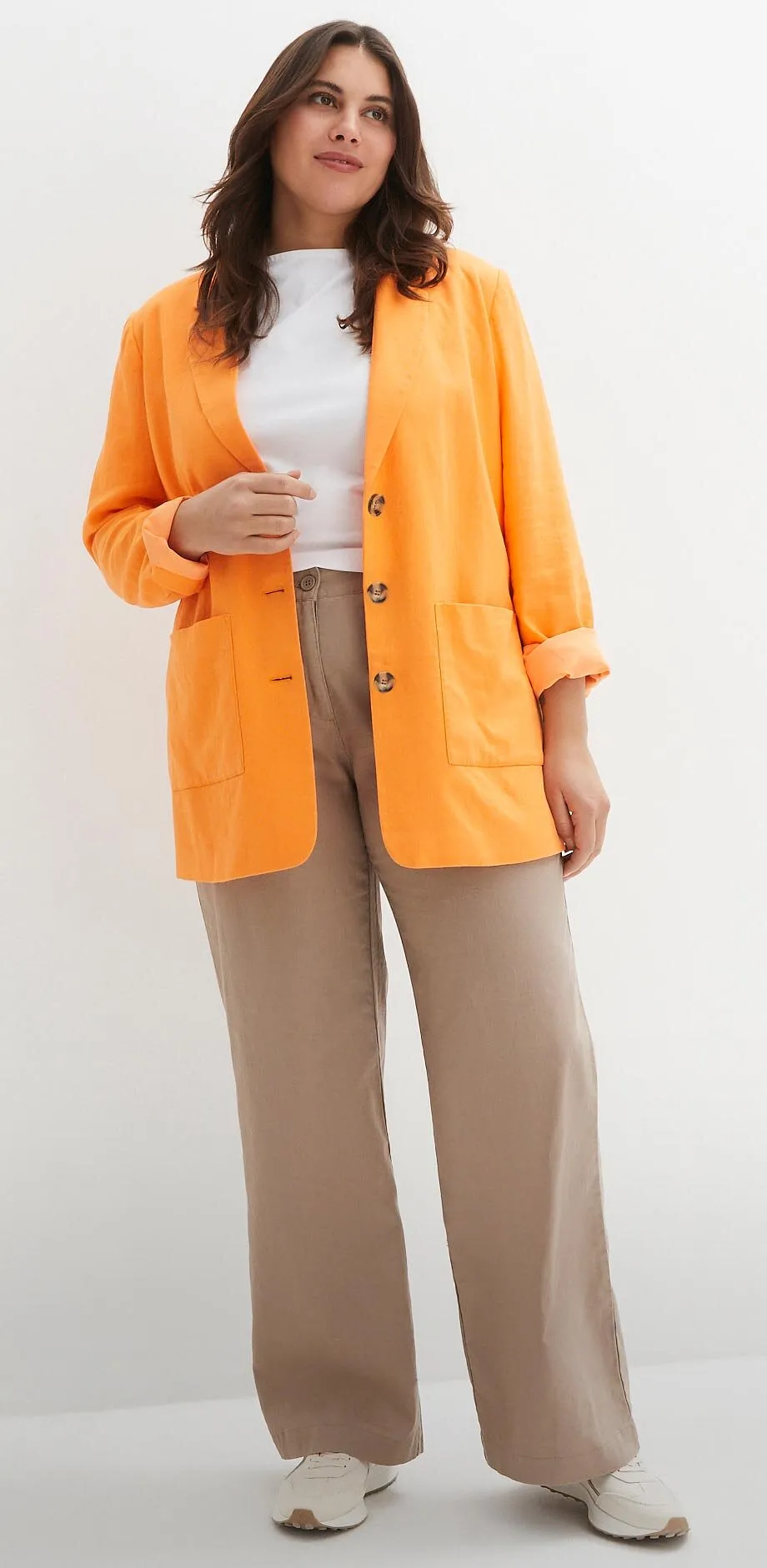 Orangefarbener Cardigan &uuml;ber wei&szlig;em Top, beige Hose und helle Schuhe.
