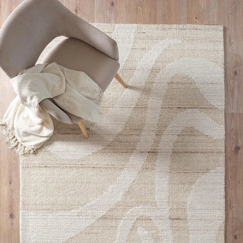 Tapis &eacute;l&eacute;gant de couleur cr&egrave;me avec des motifs abstraits, sur lequel tr&ocirc;ne un fauteuil cosy avec un plaid douillet.