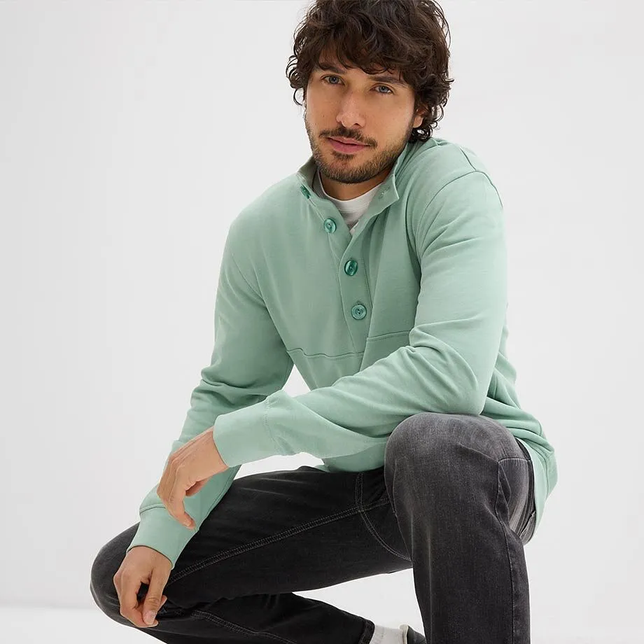 Sweat-shirt vert menthe avec patte de boutonnage, T-shirt blanc en dessous et jean de couleur fonc&eacute;e.