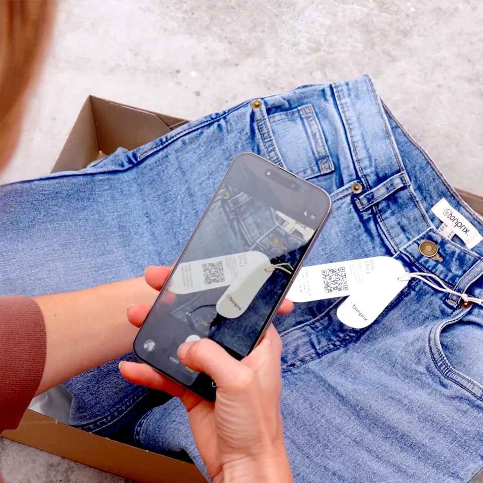 Blaue Jeans mit Etikett, neben einem Smartphone. 