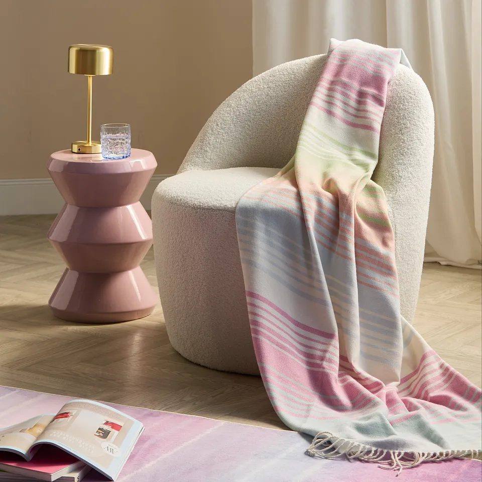 Un plaid douillet dans des teintes blanches et rose tendre d&eacute;pos&eacute; sur un fauteuil beige cosy.