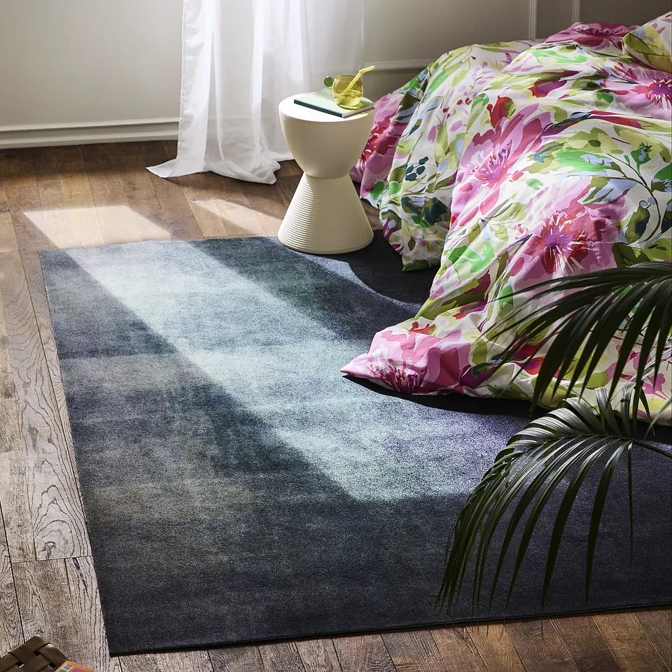 Un motif floral multicolore sur le coussin et la couverture illumine le d&eacute;cor de cette pi&egrave;ce chaleureuse dot&eacute;e d'un tapis &eacute;l&eacute;gant.