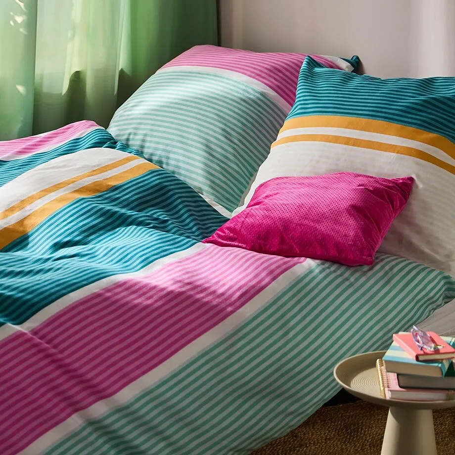 Une parure de lit multicolore &agrave; rayures rose, vert et orange d&eacute;core ce lit douillet.