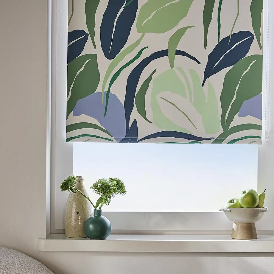 Un store &eacute;l&eacute;gant avec un motif v&eacute;g&eacute;tal en vert et bleu d&eacute;core la fen&ecirc;tre de couleur claire dans une pi&egrave;ce au style moderne.