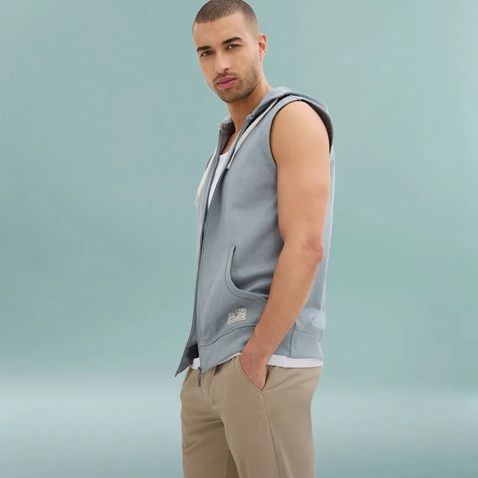 Homme v&ecirc;tu d'un gilet bleu clair en sweat &agrave; capuche par dessus un T-shirt blanc, et d'un pantalon beige.