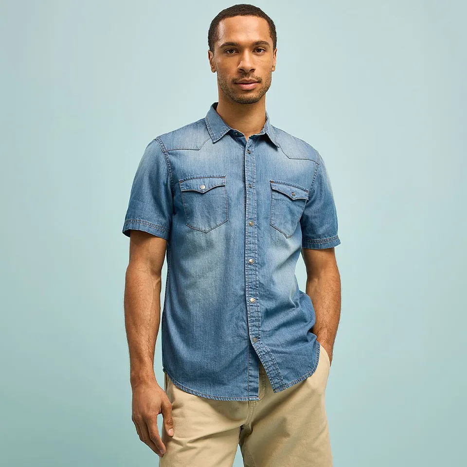 Chemise en jean bleue d&eacute;contract&eacute;e &agrave; manches courtes et pantalon beige.