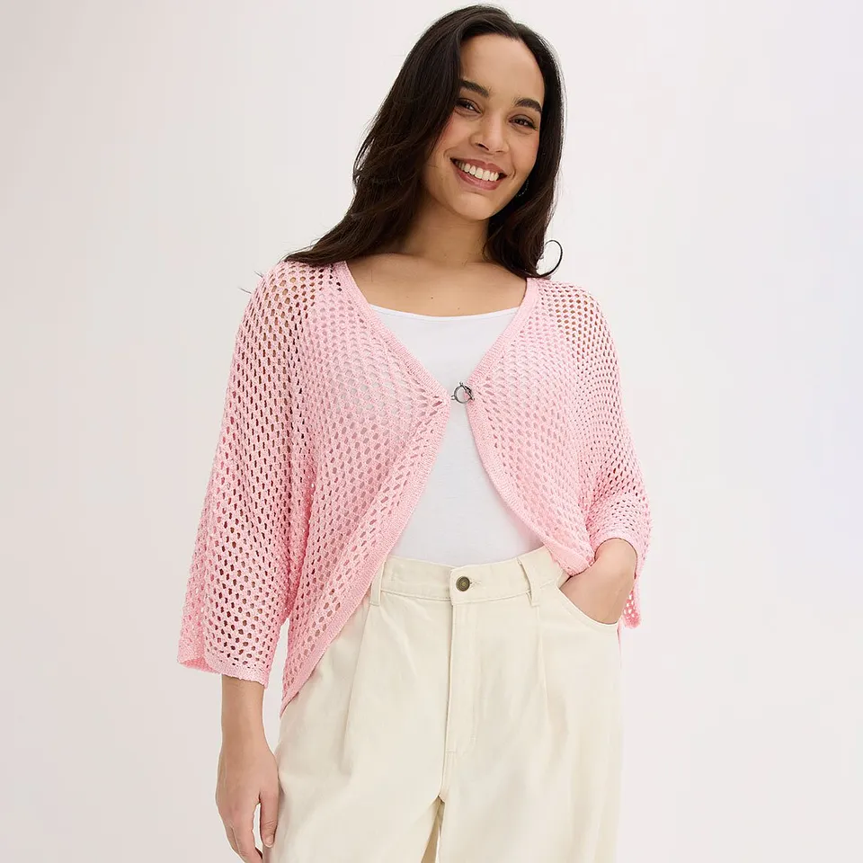 Femme v&ecirc;tue d'un gilet en maille rose sur un top blanc et d'un pantalon cr&egrave;me.