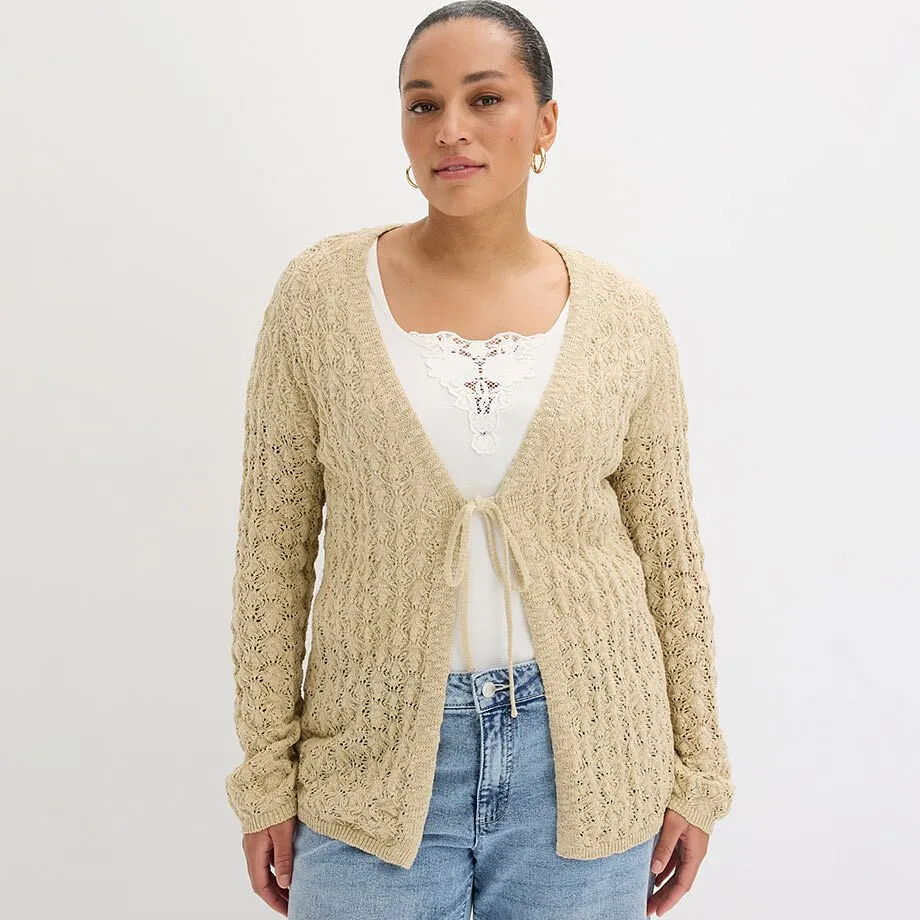 Gilet en maille beige par dessus un top blanc, associ&eacute; &agrave; un jean bleu classique.