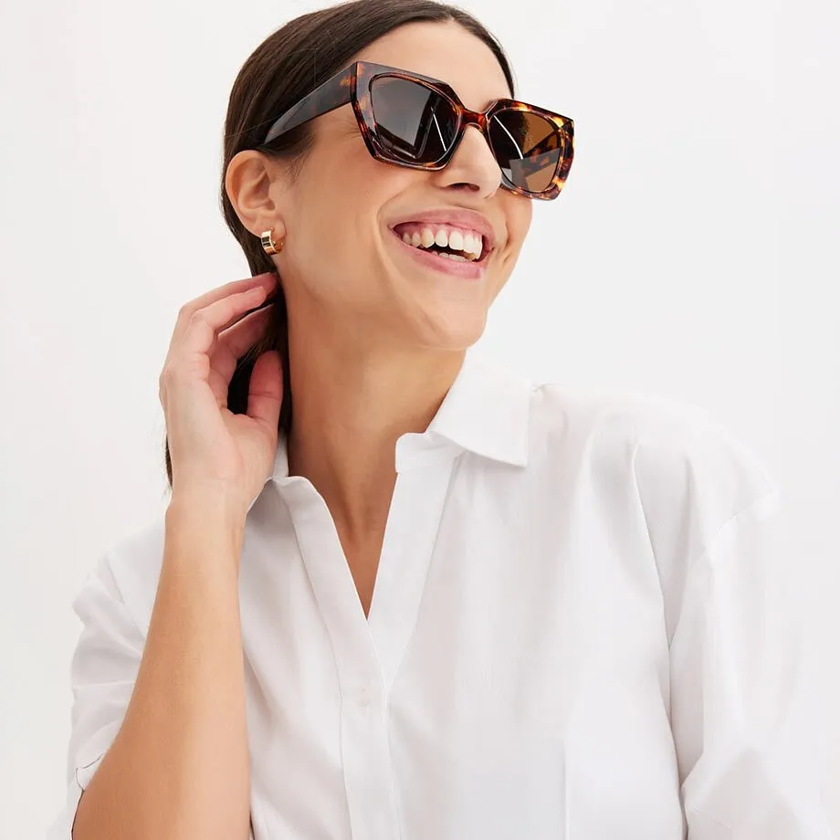 Femme v&ecirc;tue d'un chemisier blanc et portant des lunettes de soleil mode.