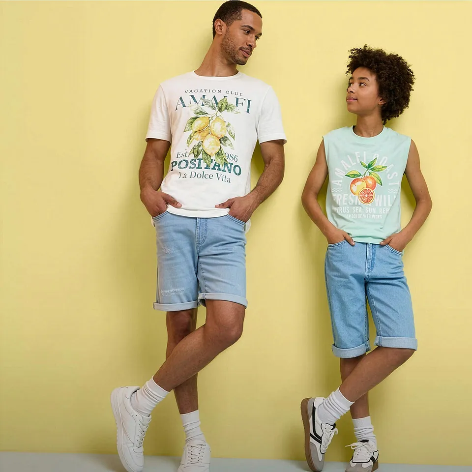 Zwei Personen tragen sommerliche Outfits mit bedruckten T-Shirts, Jeans-Shorts und wei&szlig;en Sneakers.