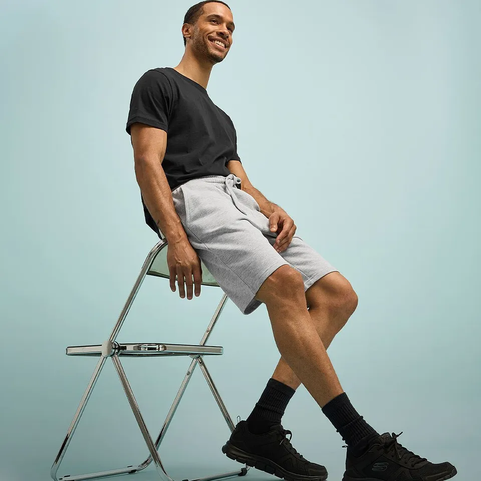 Look d&eacute;contract&eacute; avec T-shirt noir, short de couleur claire, sneakers et chaussettes fonc&eacute;es.
