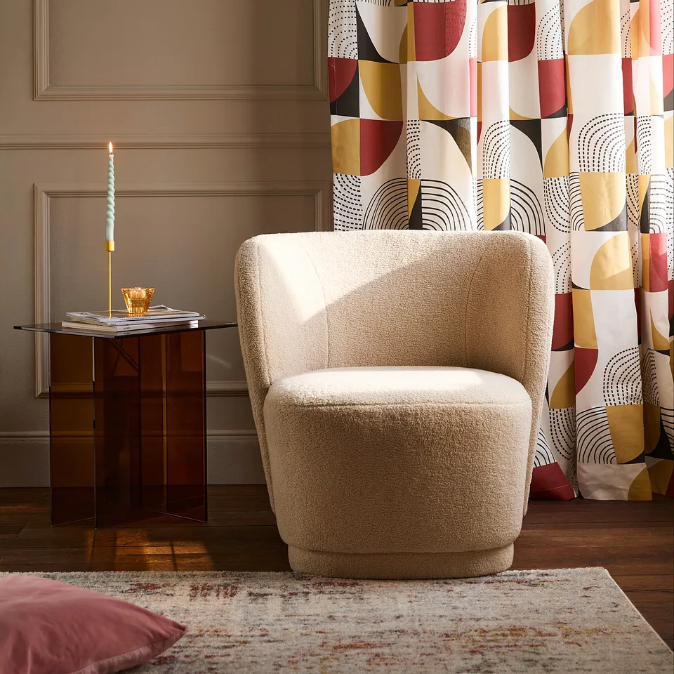 Un fauteuil beige et des rideaux aux imprim&eacute;s g&eacute;om&eacute;triques color&eacute;s cr&eacute;ent une atmosph&egrave;re moderne et chaleureuse dans la pi&egrave;ce.