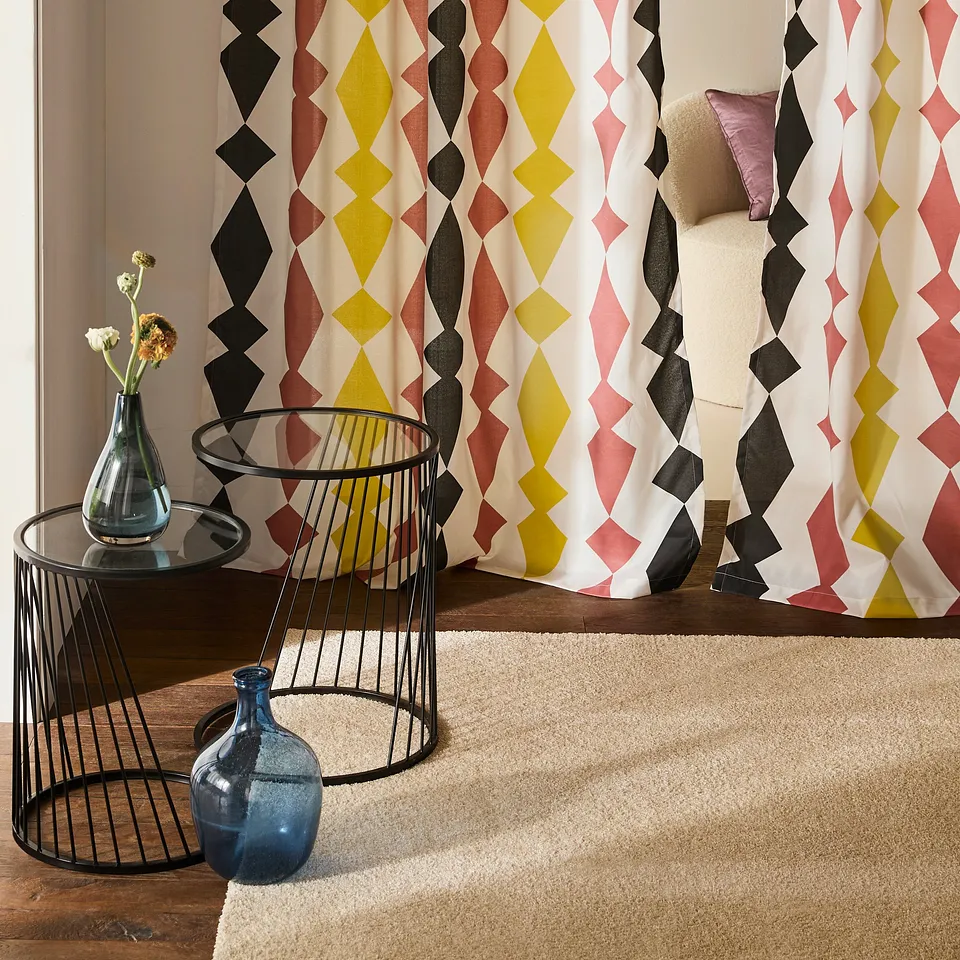 Des rideaux aux imprim&eacute;s g&eacute;om&eacute;triques color&eacute;s en forme de losanges jaune, rose et noir d&eacute;corent le salon.