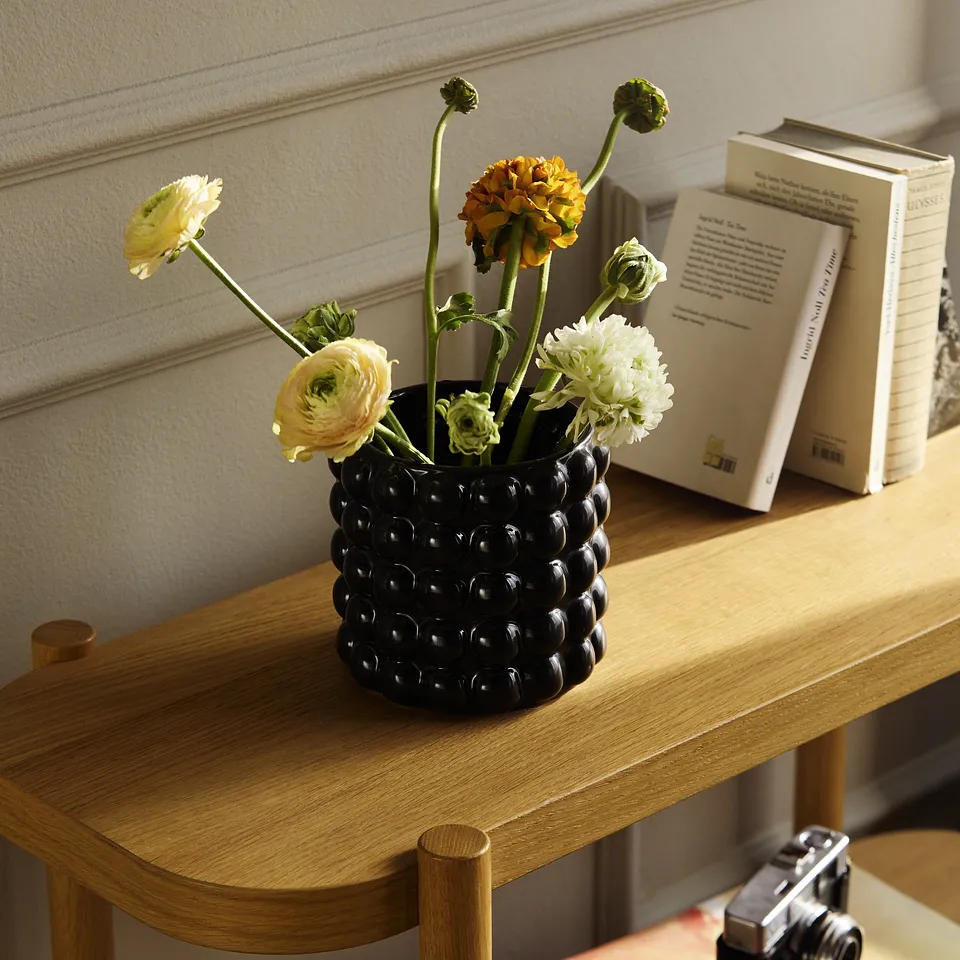 Un vase noir avec des fleurs coup&eacute;es pose un d&eacute;cor sur une table en bois o&ugrave; des livres sont pos&eacute;s.