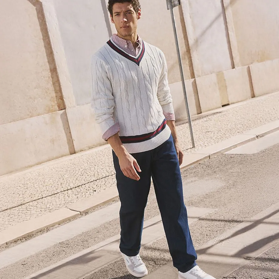 Wei&szlig;er Zopfmusterpullover &uuml;ber Hemd, dunkle Hose und wei&szlig;e Sneakers.