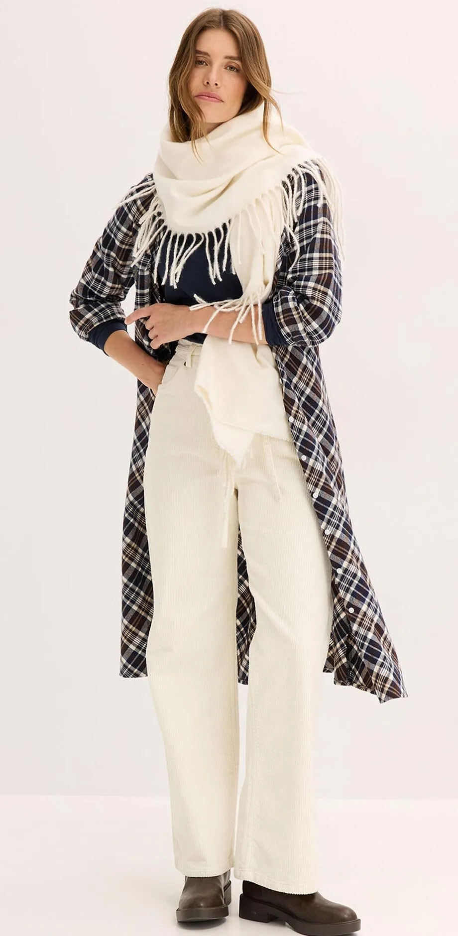 Manteau &agrave; carreaux par dessus une tenue de couleur cr&egrave;me avec un pull &agrave; col roul&eacute;, une grande &eacute;charpe et un pantalon.