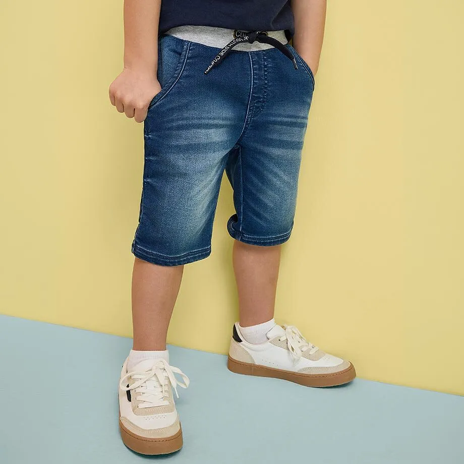 Kind tr&auml;gt blaue Jeansshorts und wei&szlig;e Sneaker.