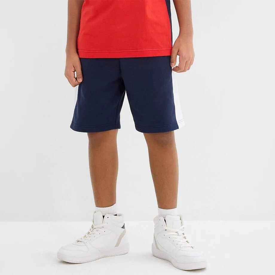 Ein Kind tr&auml;gt ein rotes Oberteil, dunkelblaue Shorts.