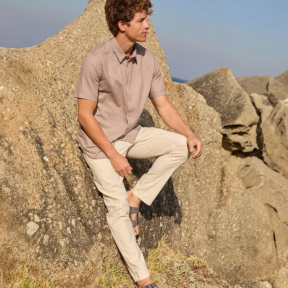 Ein Mann tr&auml;gt ein beiges Hemd und helle Chino-Hose mit Sandalen am Strand.