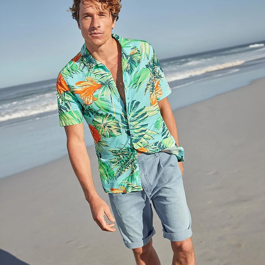 Ein Mann tr&auml;gt ein buntes Hawaiihemd und helle Shorts am Strand.