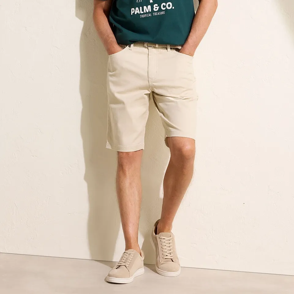 Gr&uuml;nes T-Shirt mit Aufdruck, beige Chino-Shorts und helle Sneaker.