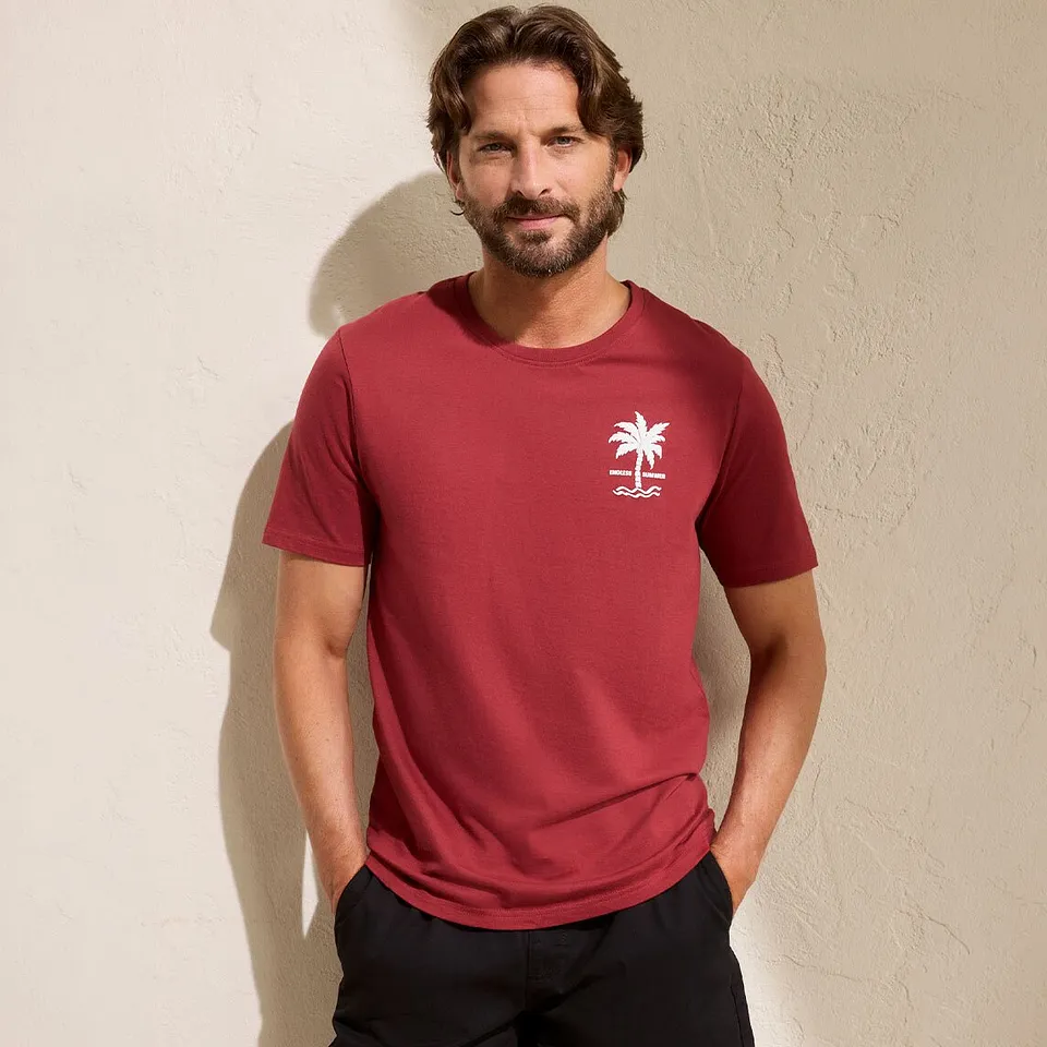 Ein Mann tr&auml;gt ein rotes T-Shirt mit kleinem wei&szlig;en Logo und schwarze Hose.