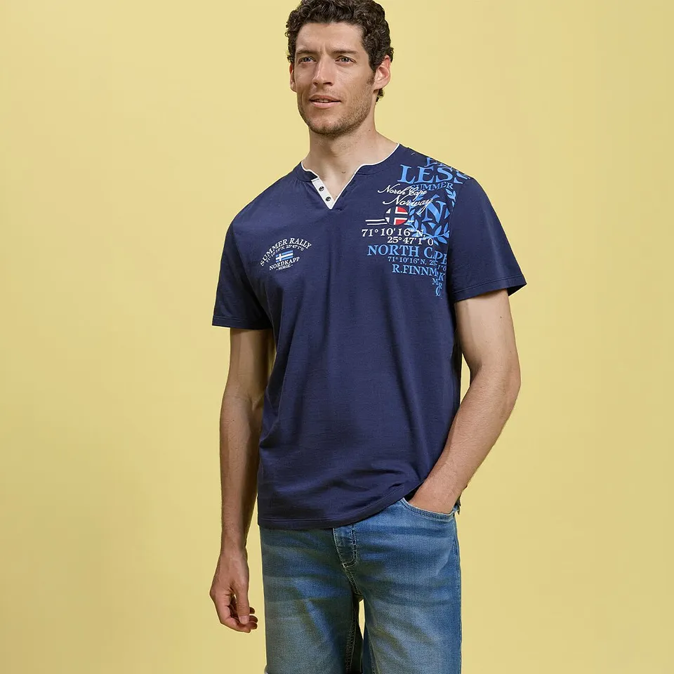 Er tr&auml;gt ein l&auml;ssiges, dunkelblaues Henley-Shirt mit auff&auml;lligem Print und helle Jeans.