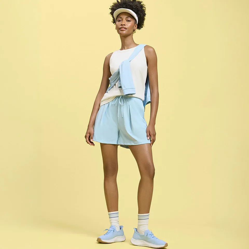 Wei&szlig;es Top, hellblaue Shorts und Pullover, dazu Sportschuhe und Schirmm&uuml;tze.