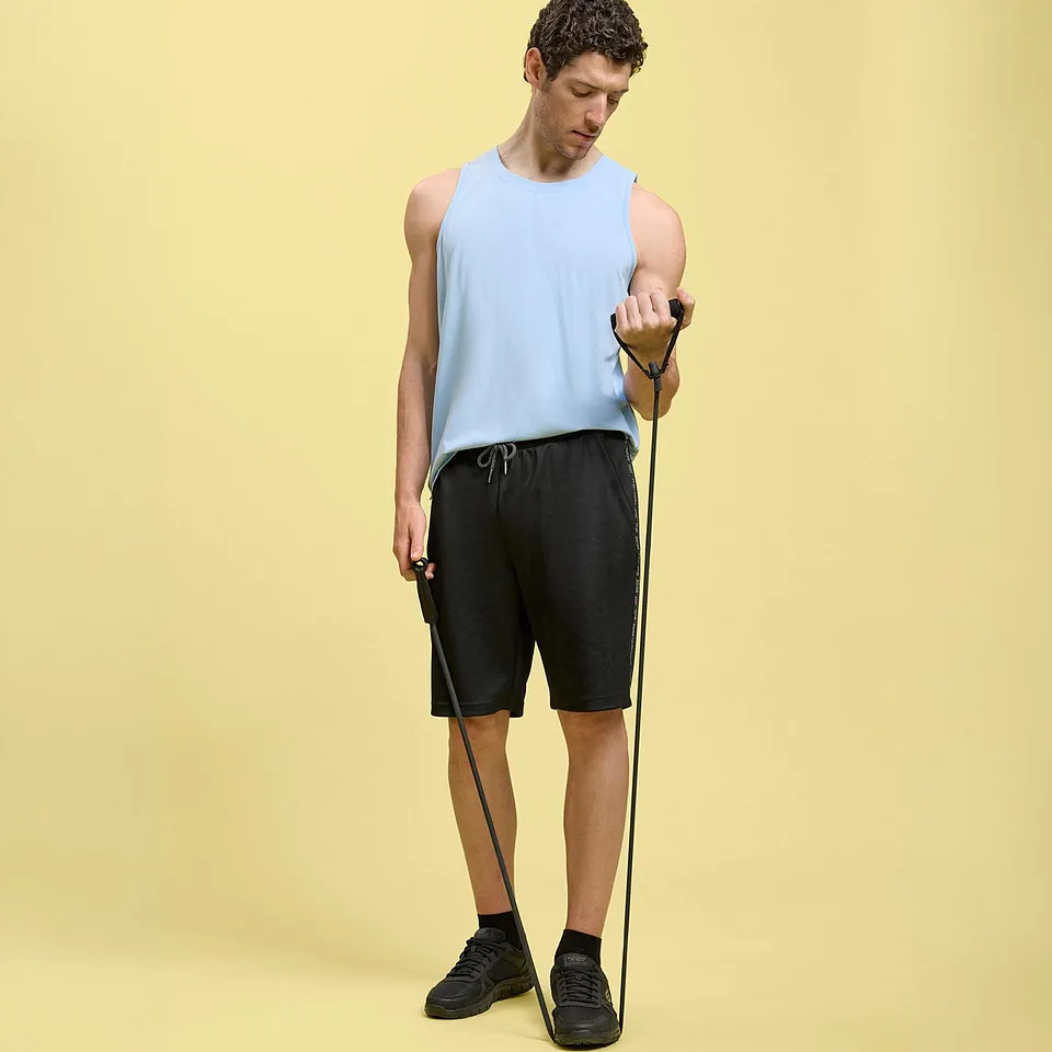 Er tr&auml;gt ein hellblaues Tanktop, schwarze Shorts und dunkle Sportschuhe.