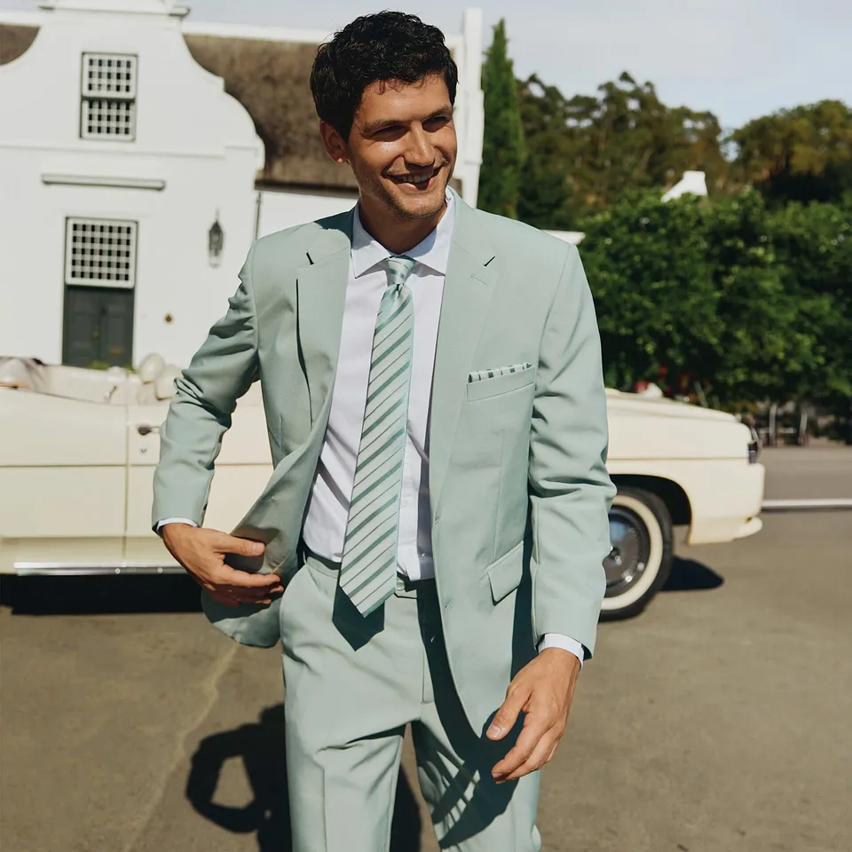 Homme &eacute;l&eacute;gant en costume vert clair, chemise blanche et cravate ray&eacute;e coordonn&eacute;e.