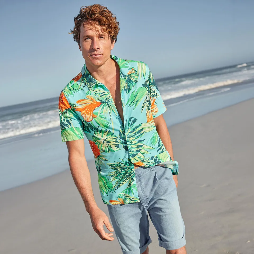 Un homme v&ecirc;tu d'une chemise hawa&iuml;enne multicolore et d'un short de couleur claire sur la plage.