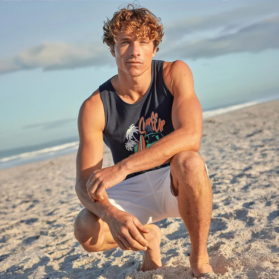 Un homme sur la plage portant un d&eacute;bardeur bleu &agrave; motif et un short blanc.