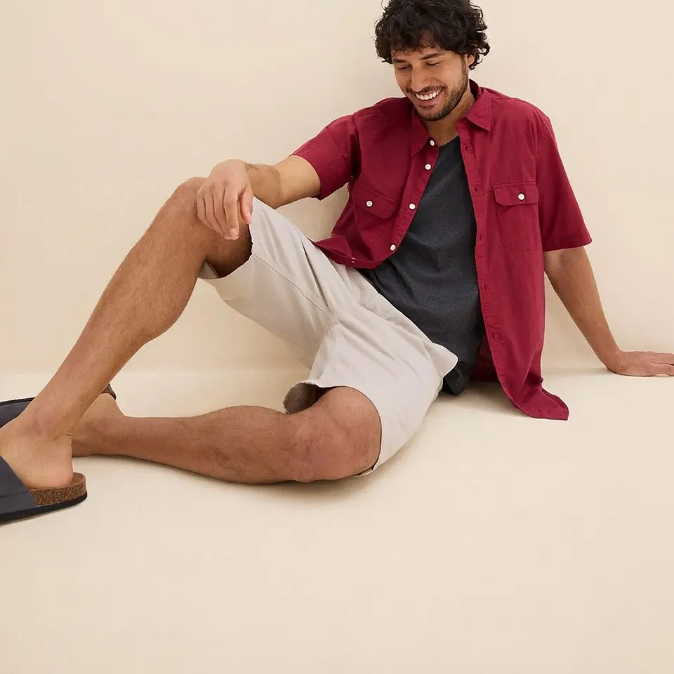 Chemise rouge &agrave; manches courtes sur un T-shirt fonc&eacute;, bermuda de couleur claire et sandales confortables.