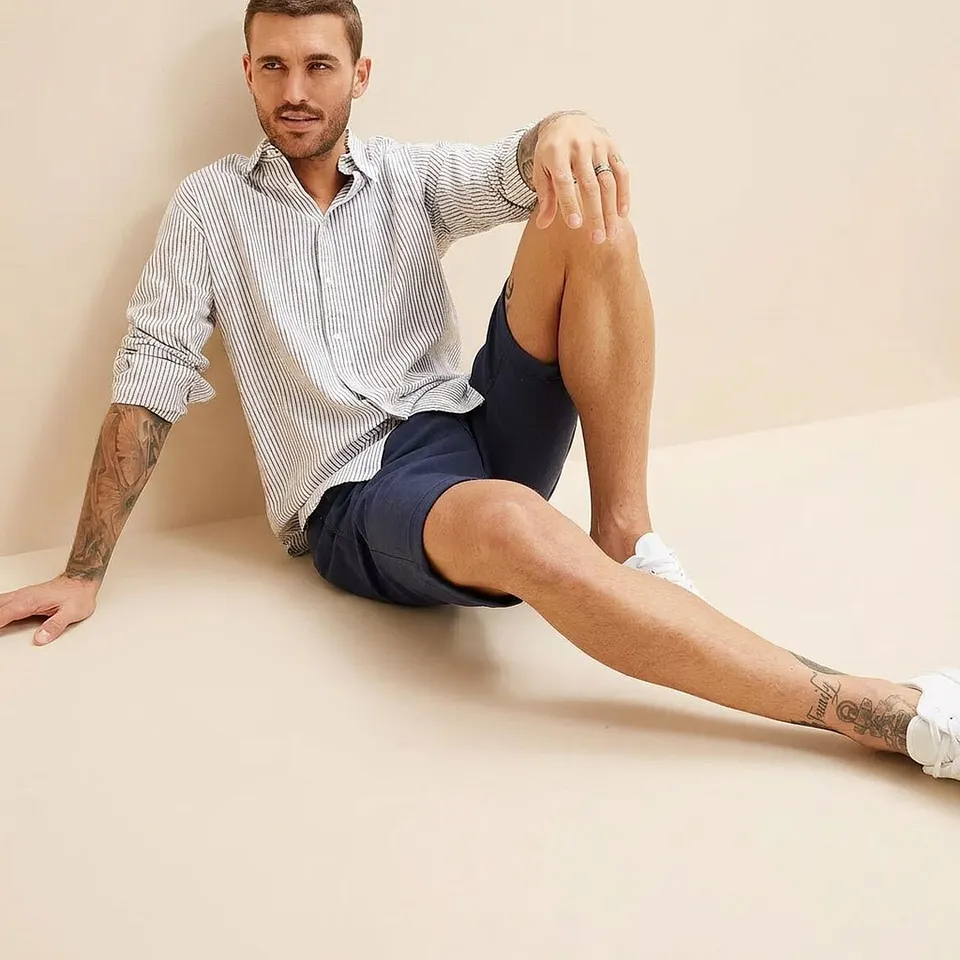 Un homme portant une chemise ray&eacute;e, un short bleu fonc&eacute; et des baskets blanches.