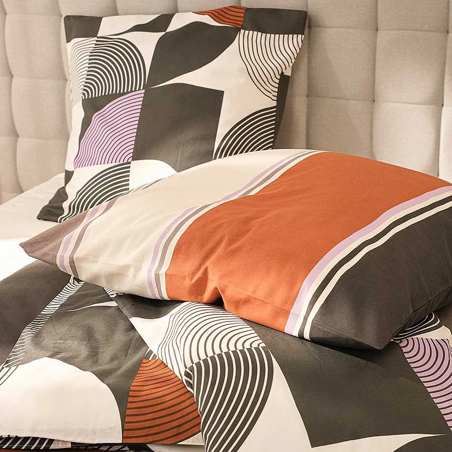 Linge de lit &agrave; motif g&eacute;om&eacute;trique en gris, orange, blanc et lilas.