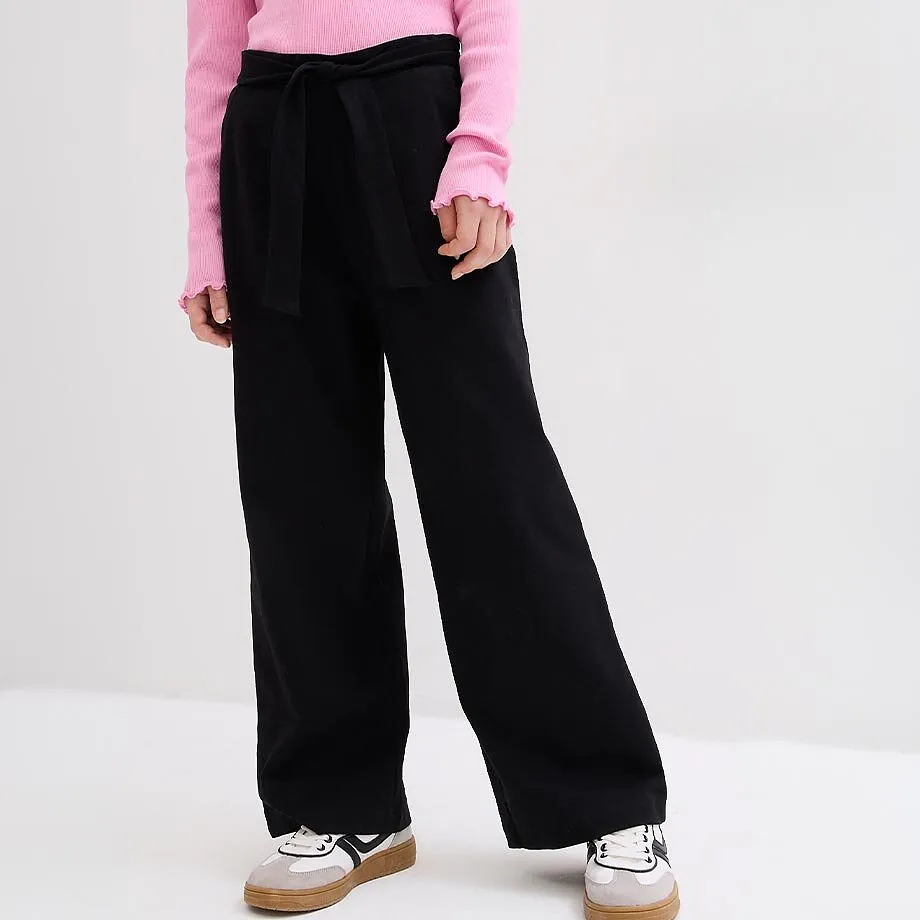 Haut rose, pantalon large noir avec cordon et baskets.