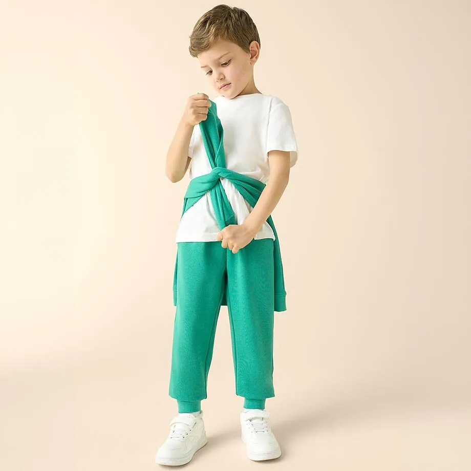Kind in wei&szlig;em T-Shirt, gr&uuml;ner Hose und umgebundenem Pullover.