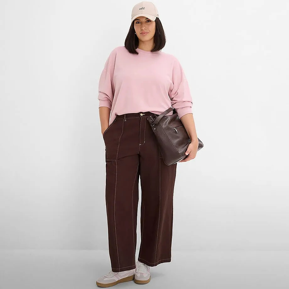 Sweat-shirt rose, pantalon large marron avec coutures, casquette beige et sac fonc&eacute;.