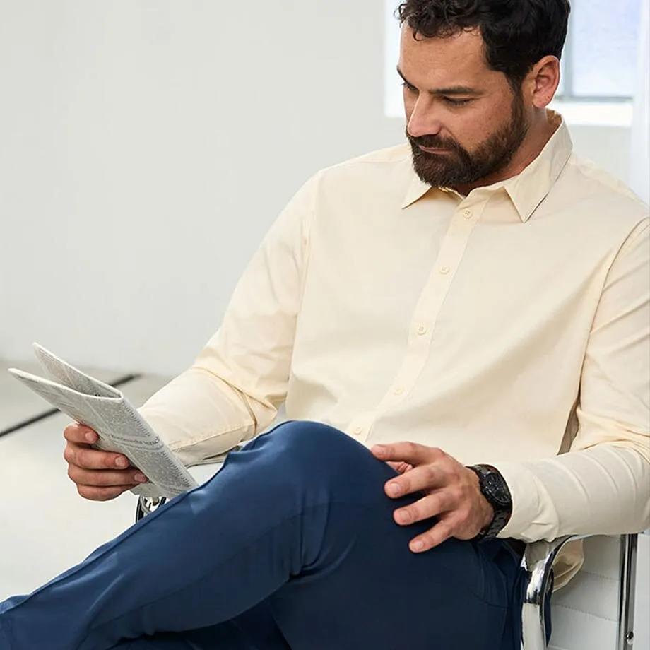 Der Mann tr&auml;gt ein beigefarbenes Hemd, dunkelblaue Hose und eine schwarze Armbanduhr.