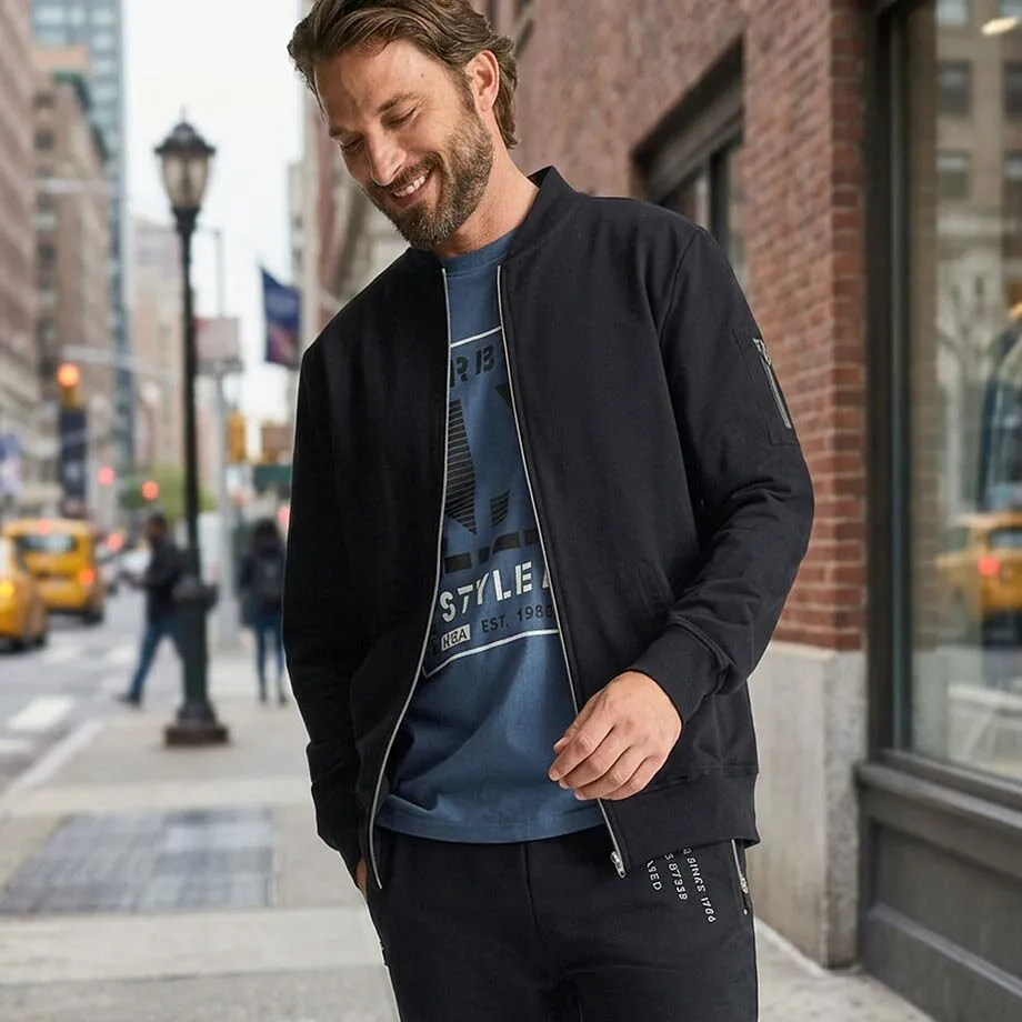 Schwarze Bomberjacke, blaues Shirt, dunkle Hose und wei&szlig;e Sneaker.