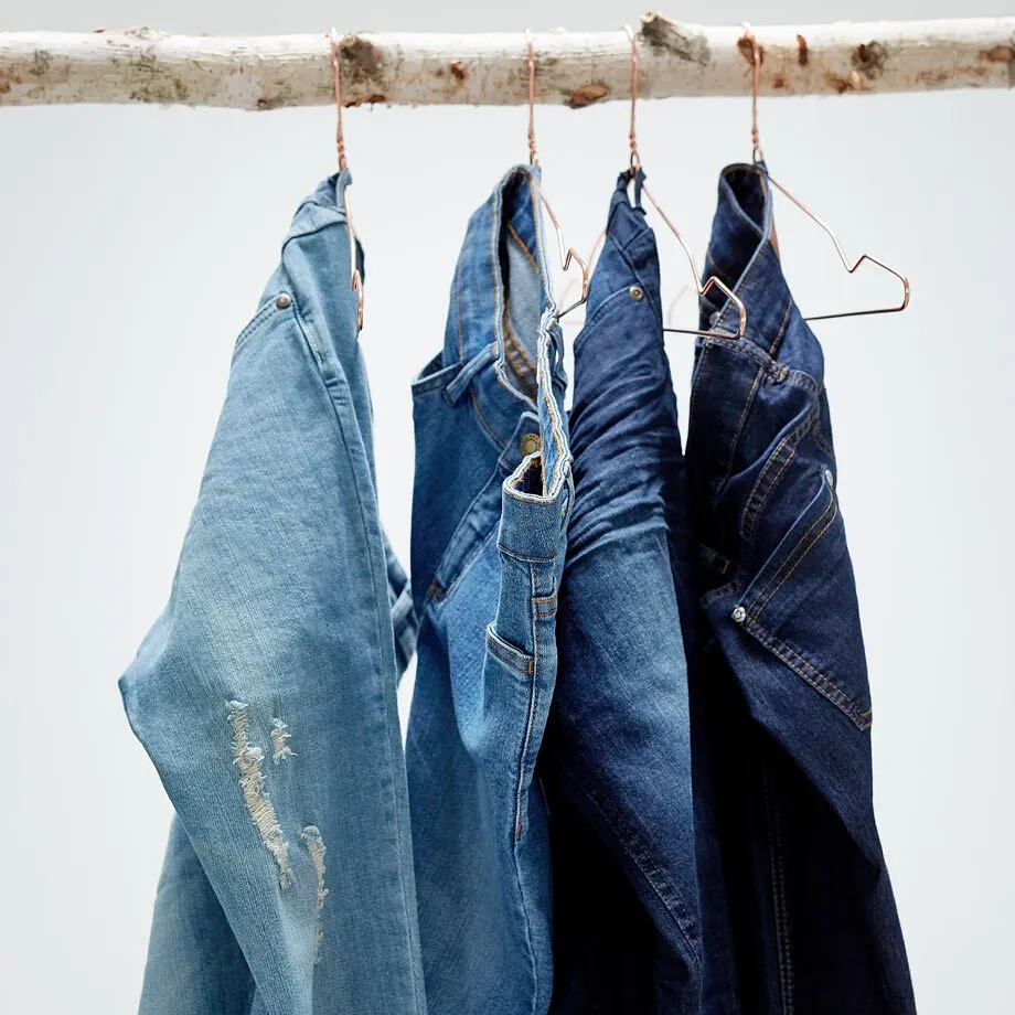 Jeans in verschiedenen Blaut&ouml;nen h&auml;ngen an B&uuml;geln auf einem Holzast.