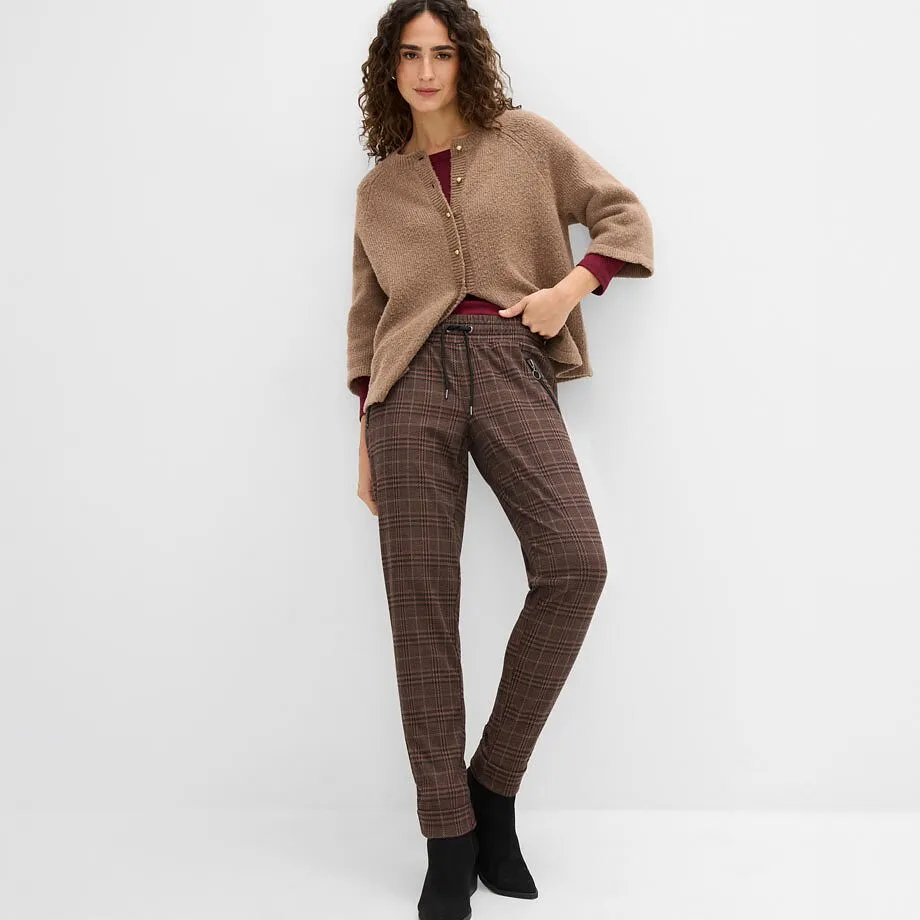 Braune Strickjacke, rotes Oberteil, karierte Hose und schwarze Stiefeletten.