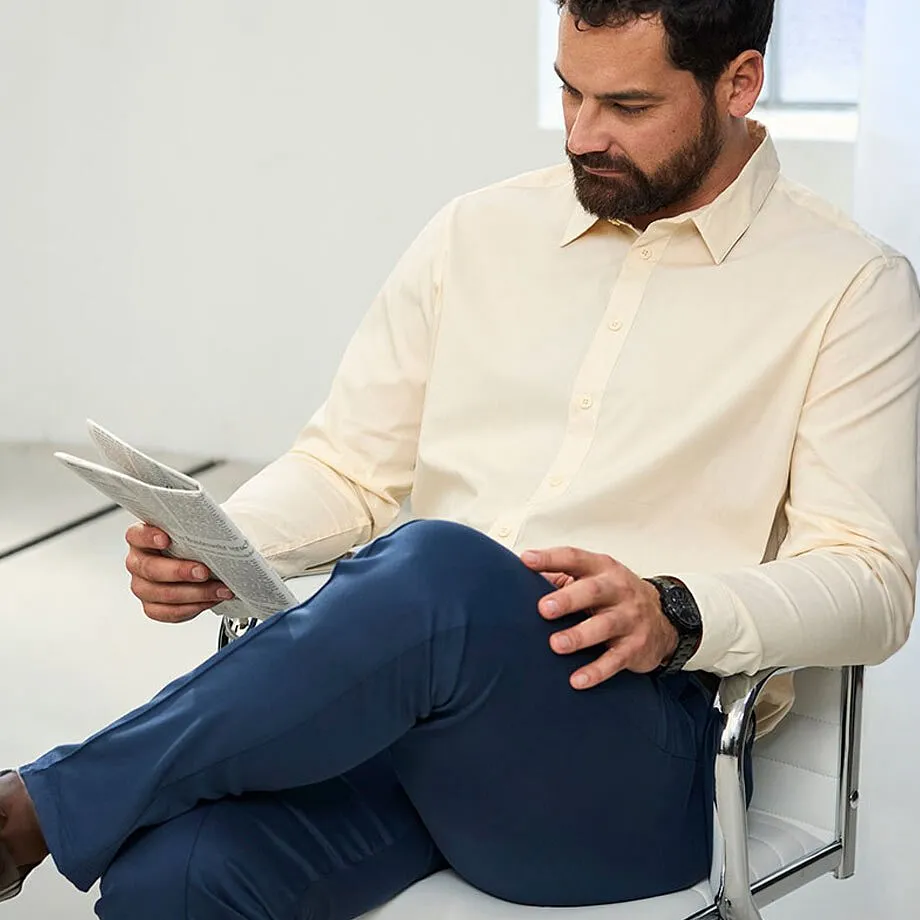 Un homme v&ecirc;tu d'une chemise beige, un pantalon bleu fonc&eacute; et portant une montre noire au poignet.