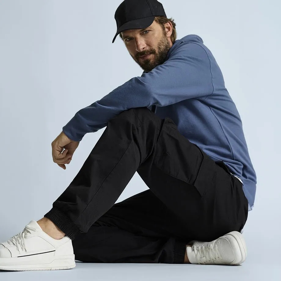 Look d&eacute;contract&eacute; : casquette noire, pull &agrave; capuche bleu, pantalon cargo noir confortable et sneakers blanches.