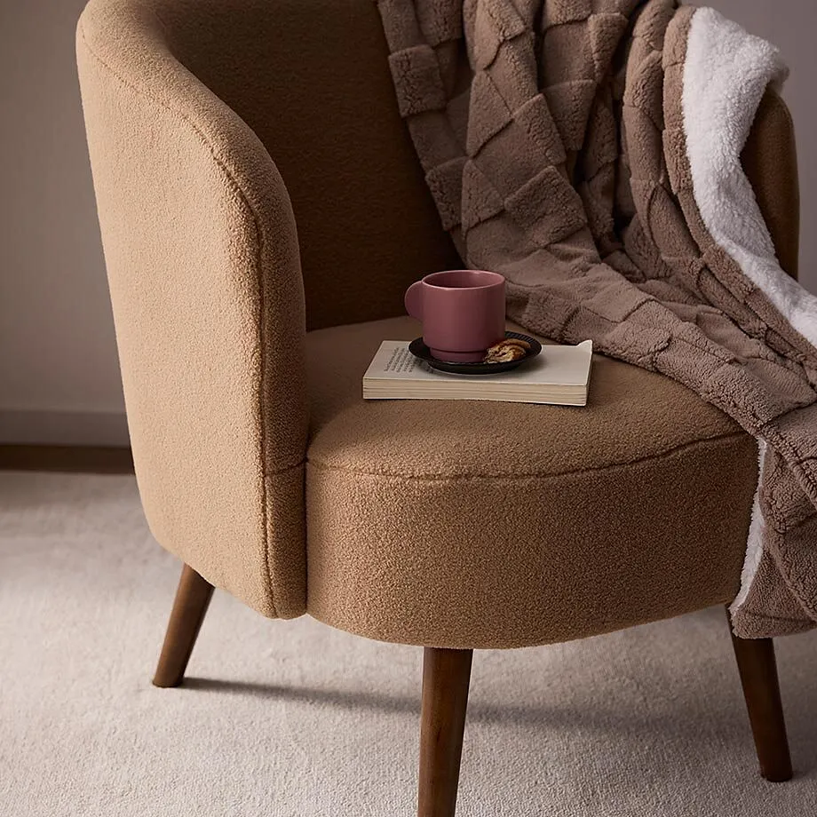 Fauteuil douillet avec couverture marron, livre et tasse.